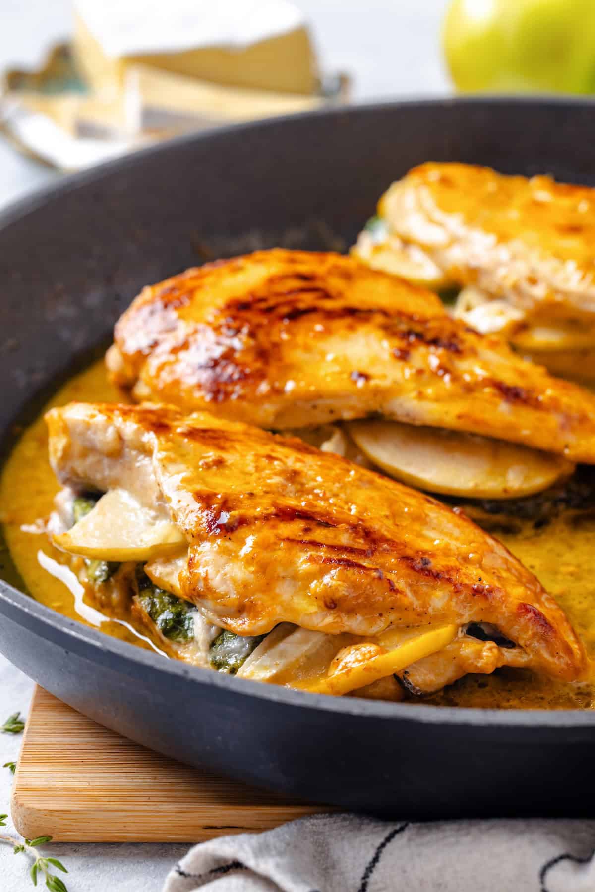 Close up of apple and brie stuffed chicken breasts seared and cooked in a pan sauce in a skillet.