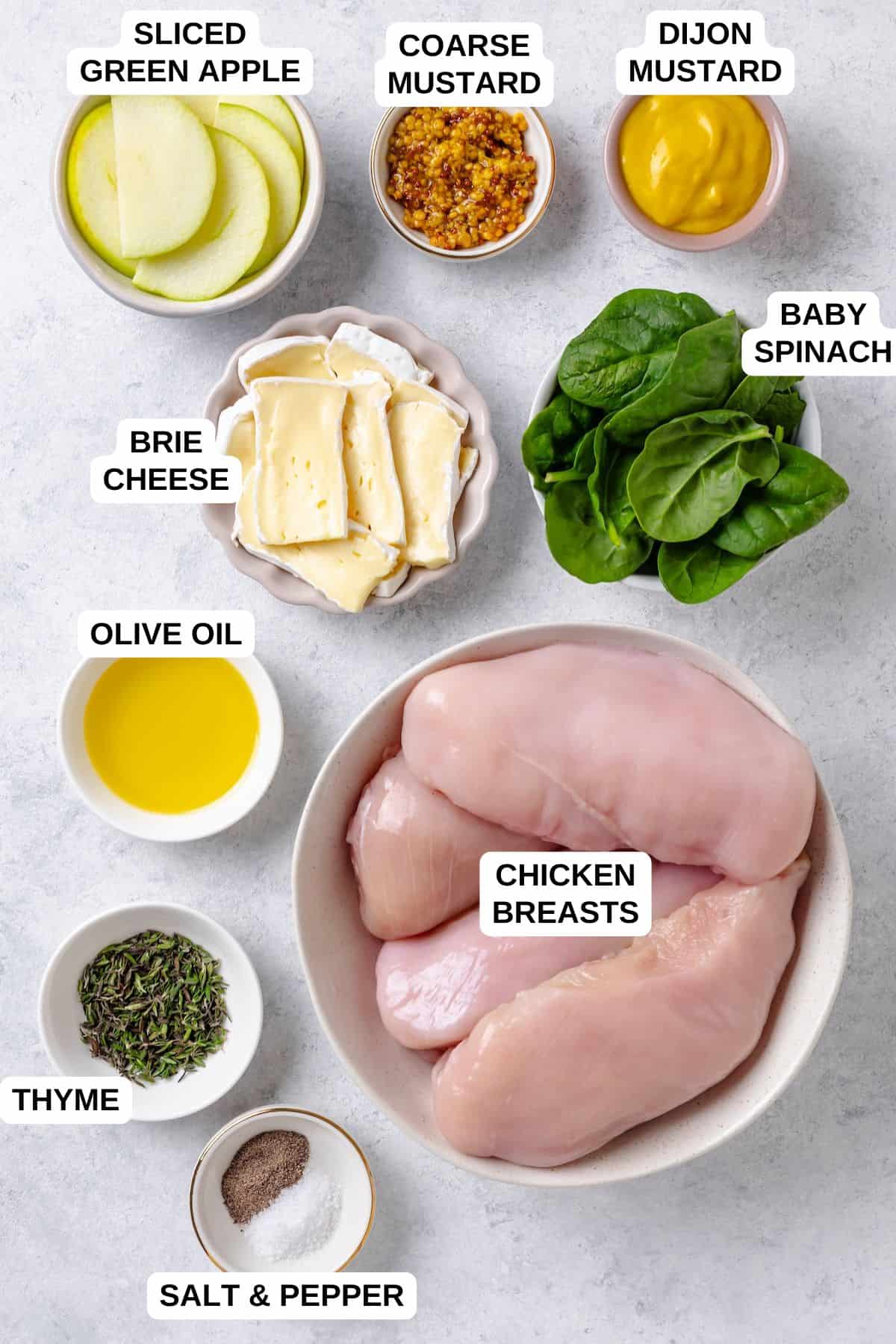 Ingredients laid out in separate bowls for making a chicken recipe with spinach, brie cheese and sliced apples.