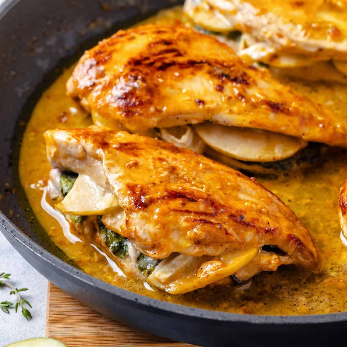 Close up of apple and brie stuffed chicken breasts in a pan sauce in a large dark skillet.