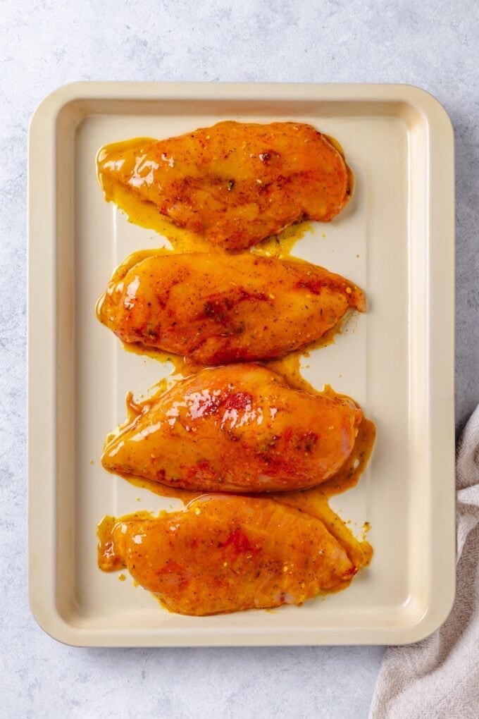Chicken breasts laid out on a sheet pan with a honey mustard sauce on top.