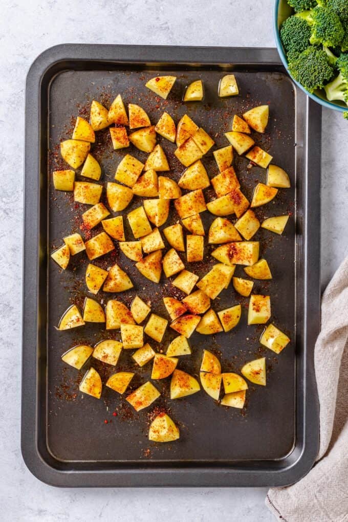 Diced potatoes with seasoning spread out on a sheet pan before being cooked.