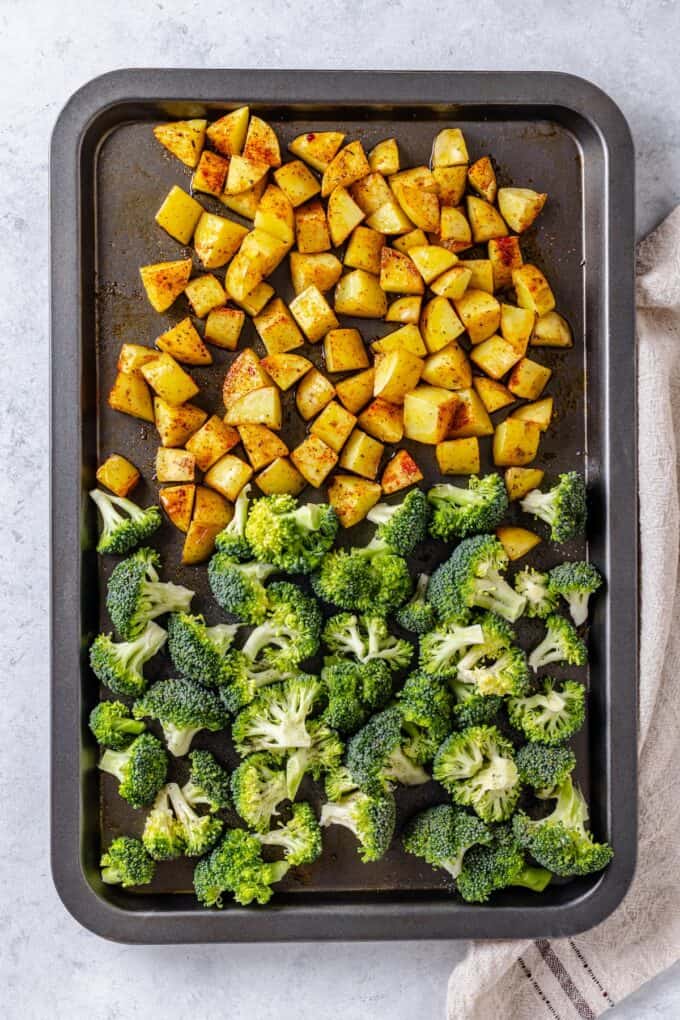 Diced potatoes with seasoning and broccoli florets on a sheet pan.