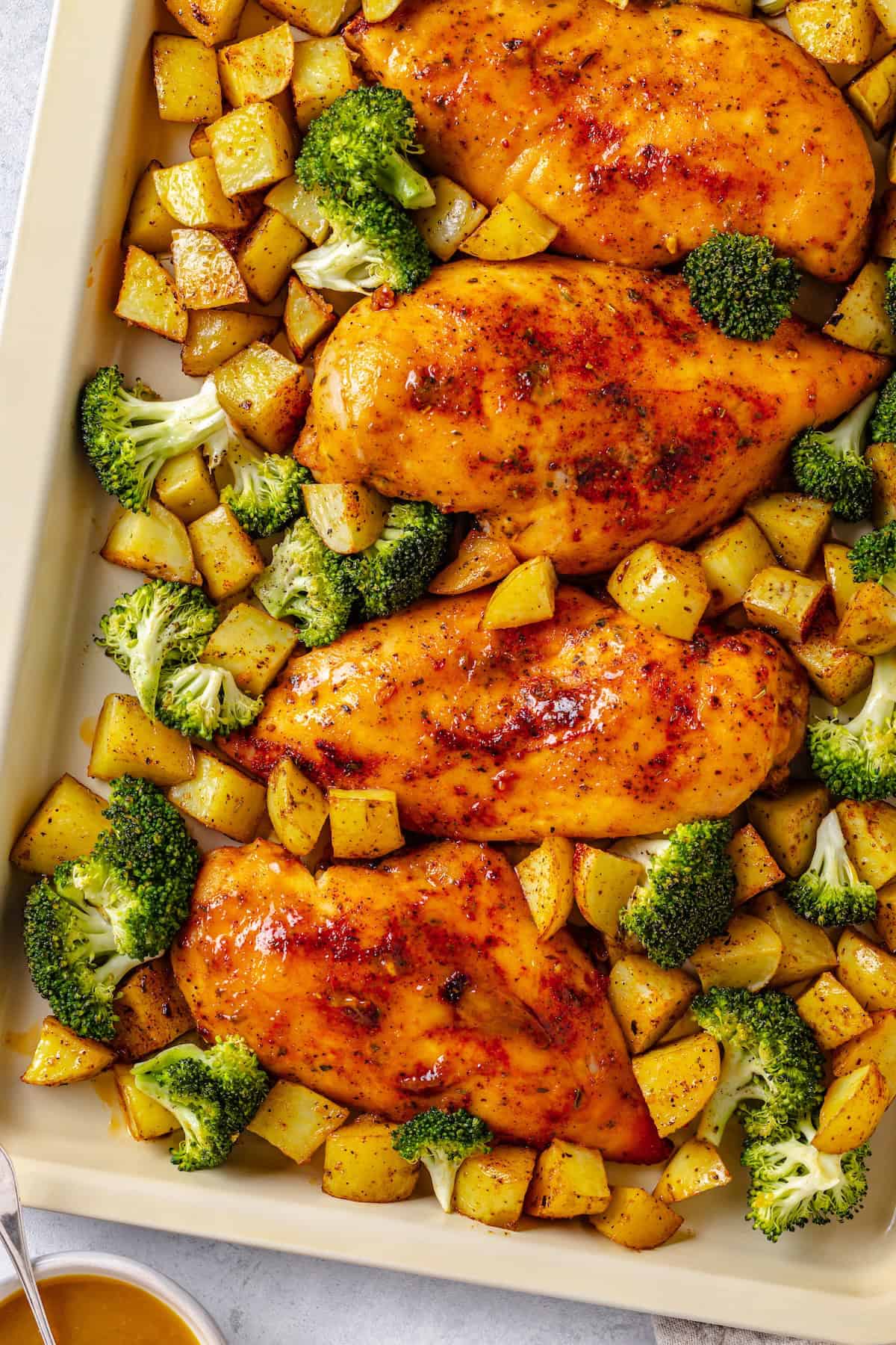 A sheet pan with honey mustard chicken with potatoes and broccoli.