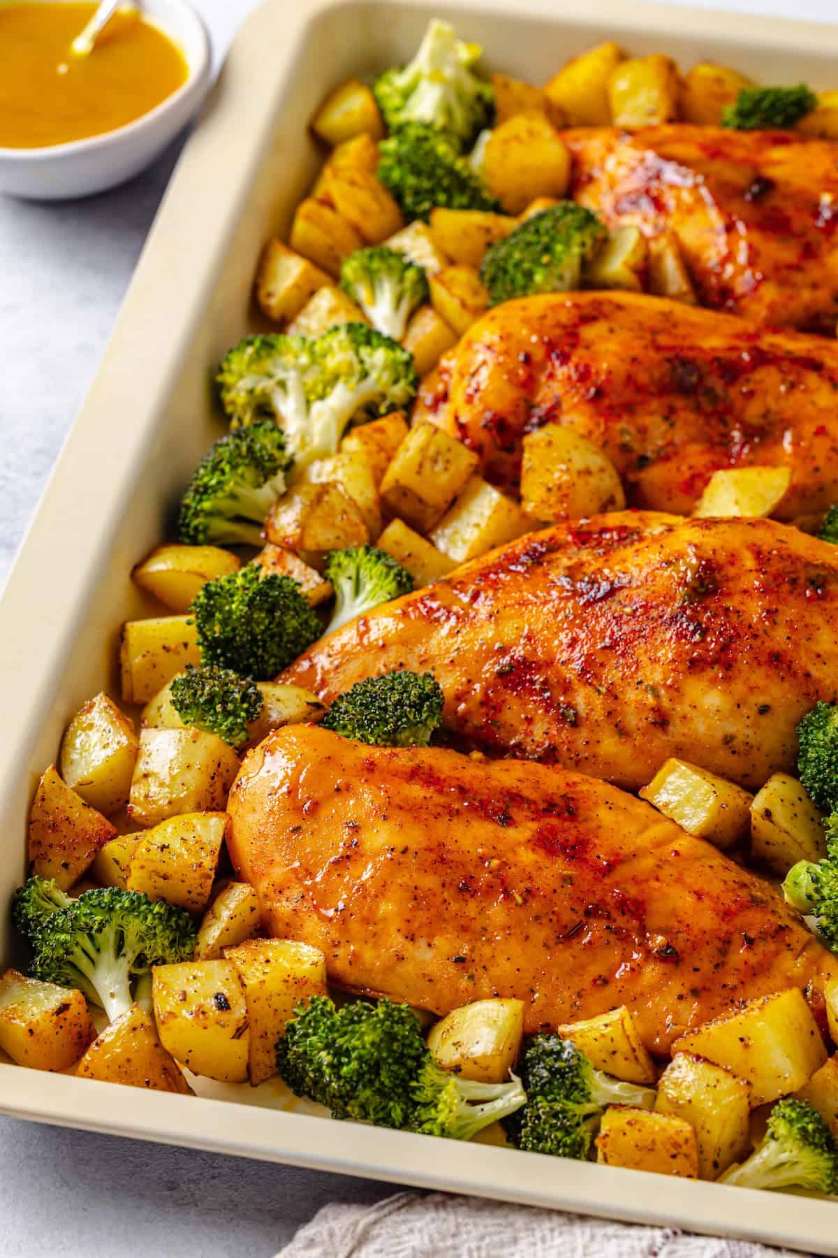 Honey mustard chicken breasts on a sheet pan nestled in among broccoli florets and potato cubes.
