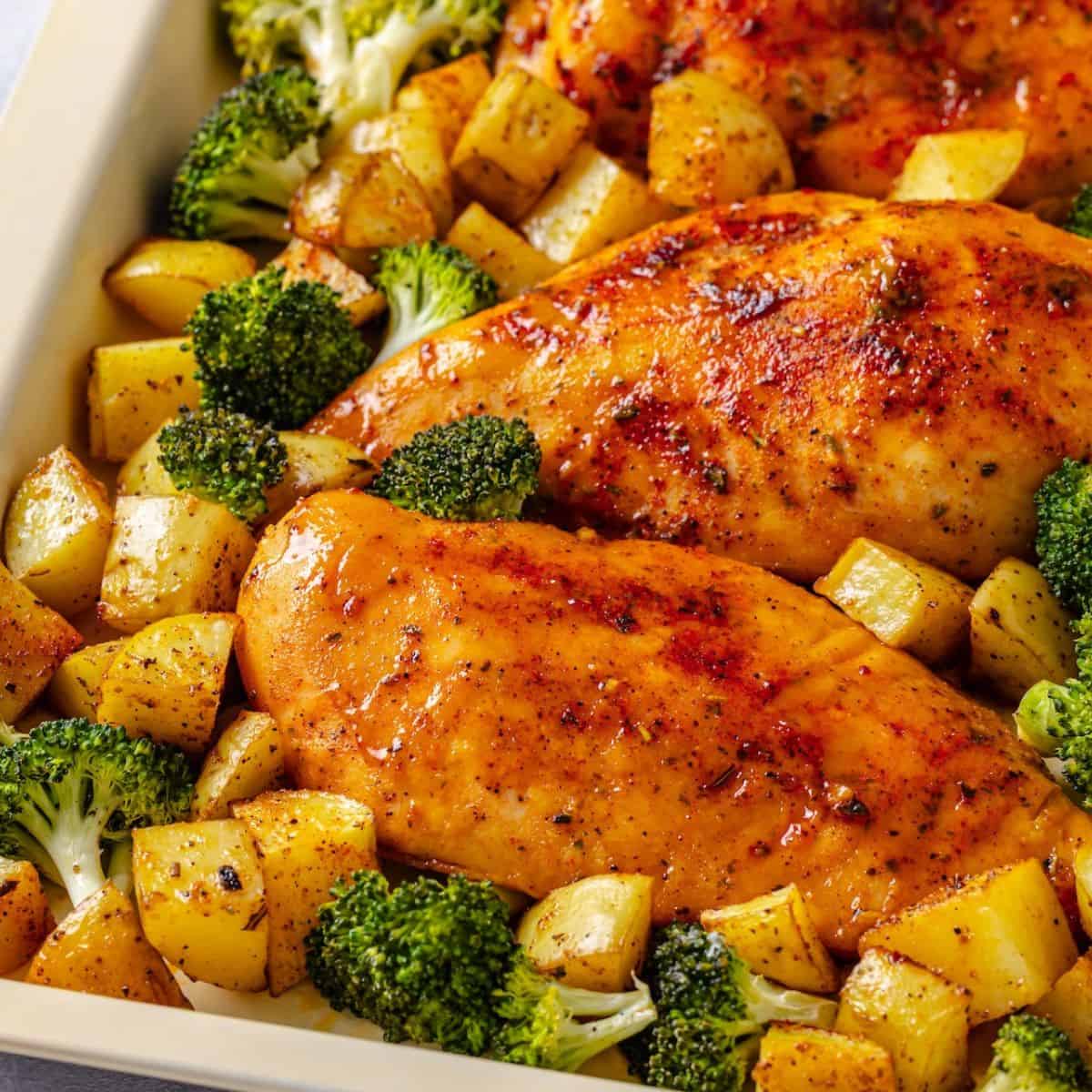 Close up of honey mustard chicken breasts on a sheet pan nestled in among broccoli florets and potato cubes.