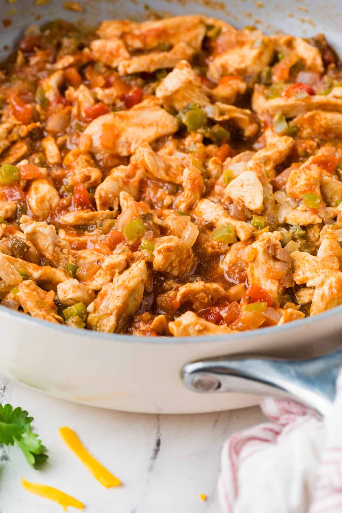 A large skillet with a mixture of sliced chicken, onions, peppers and salsa.