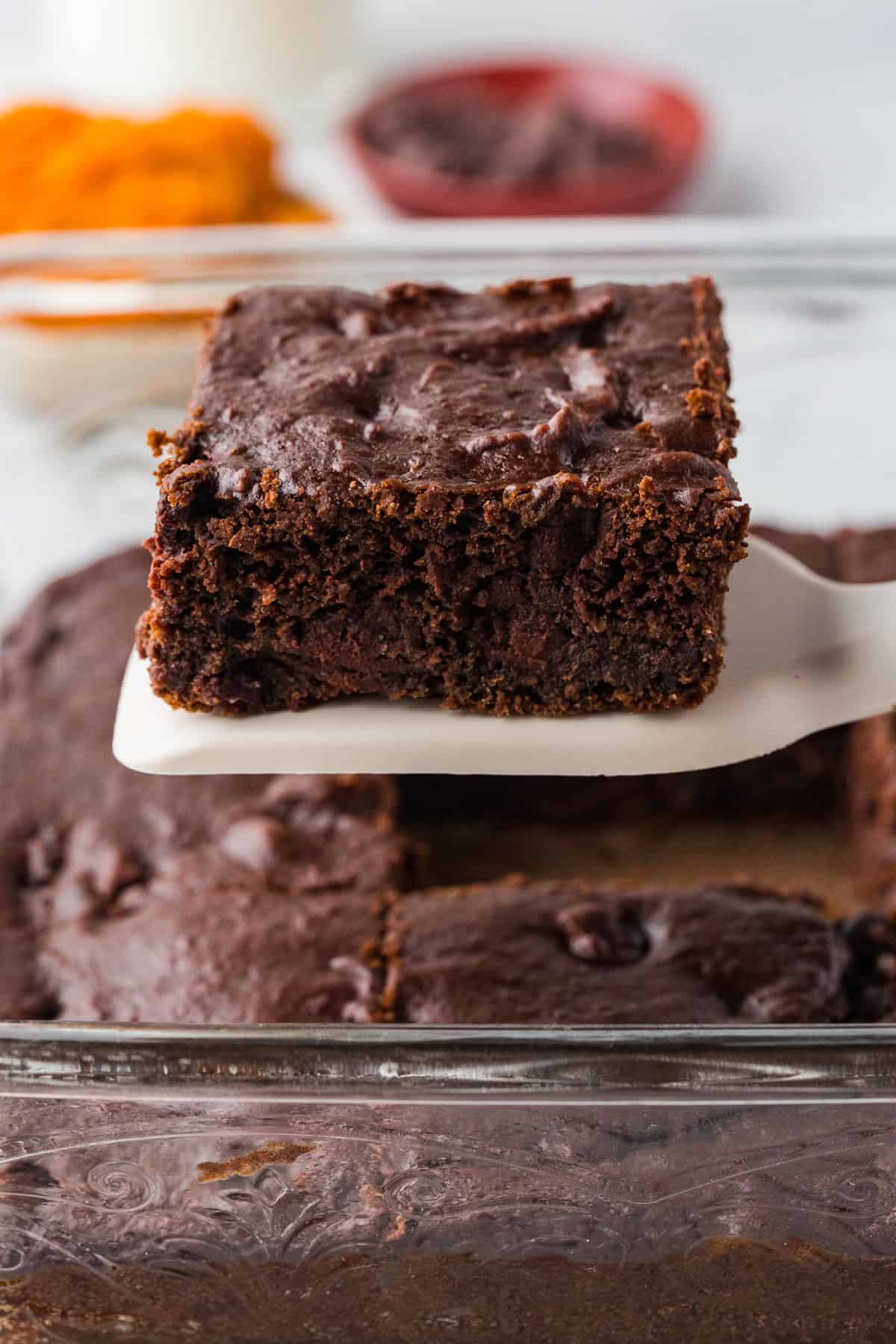 A square piece of chocolate pumpkin cake being lifted up from a baking dish.