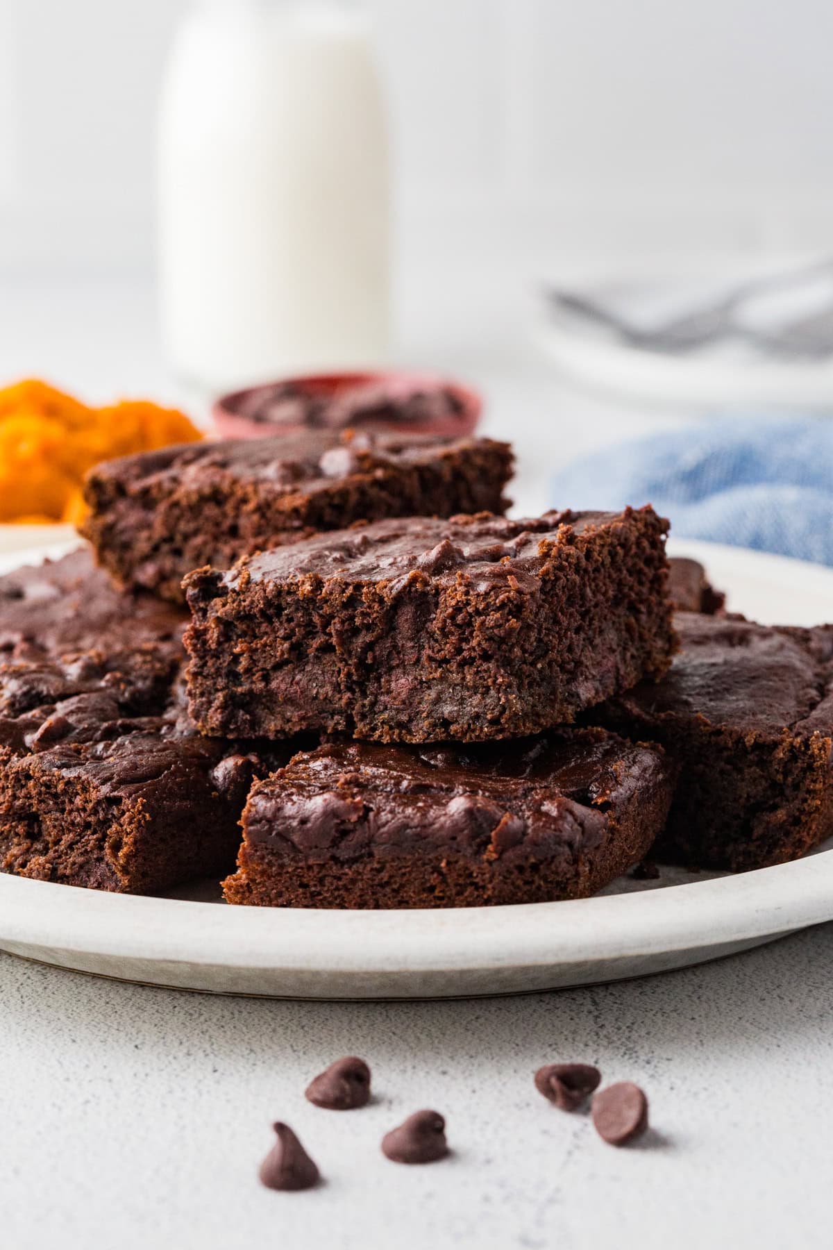 A plate full of square cut slices of chocolate pumpkin cake with chocolate chips with a pitcher of milk in the background.