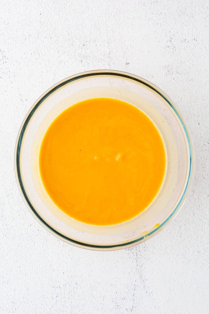 A clear glass bowl with a wet pumpkin and milk mixture.