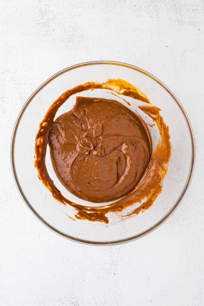 A fudgy chocolate batter stirred together in a glass bowl.