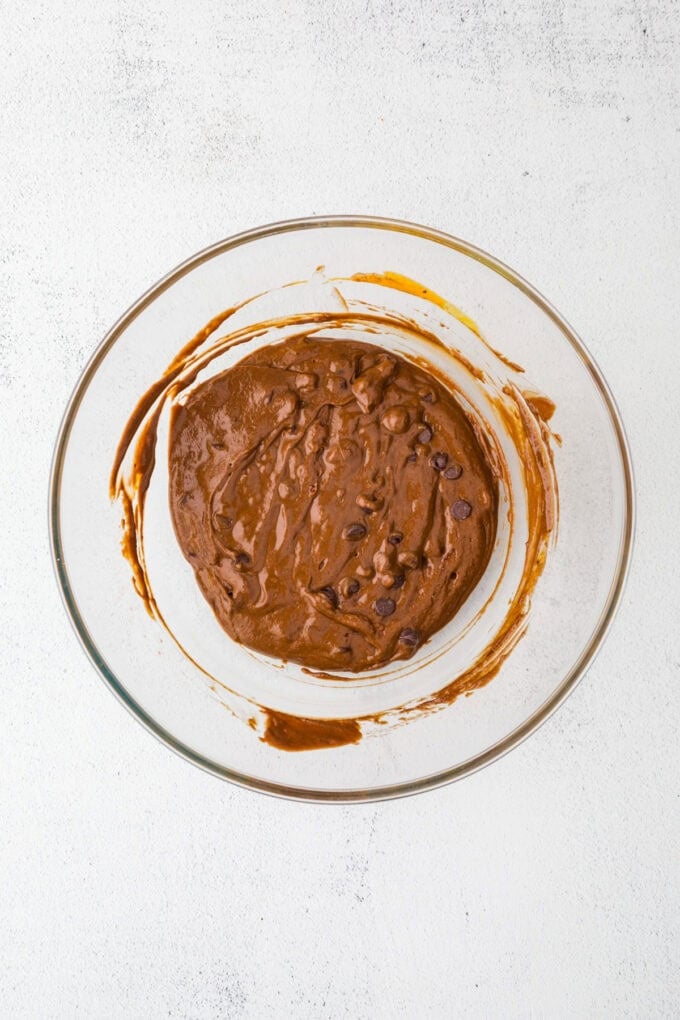 A fudgy chocolate batter with chocolate chips stirred together in a glass bowl.
