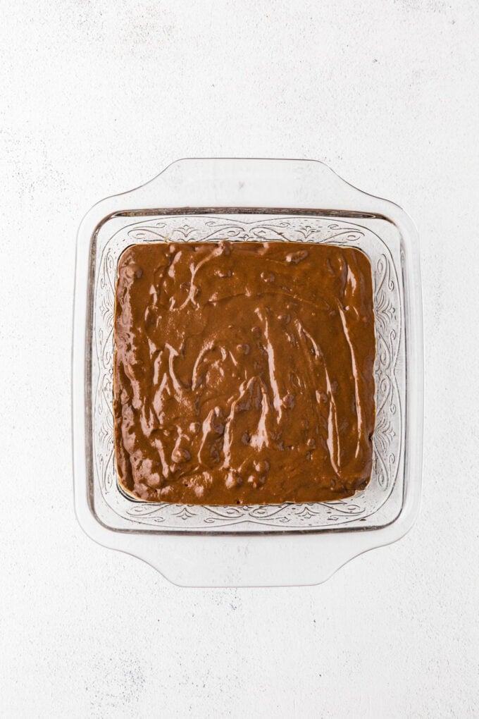 A square glass baking dish filled with a chocolate batter with chocolate chips before being baked.