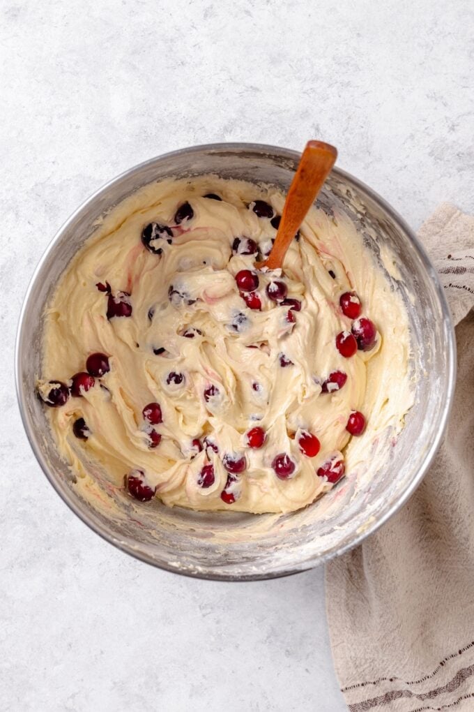 Fresh cranberries folded into a cake batter in a silver mixing bowl.