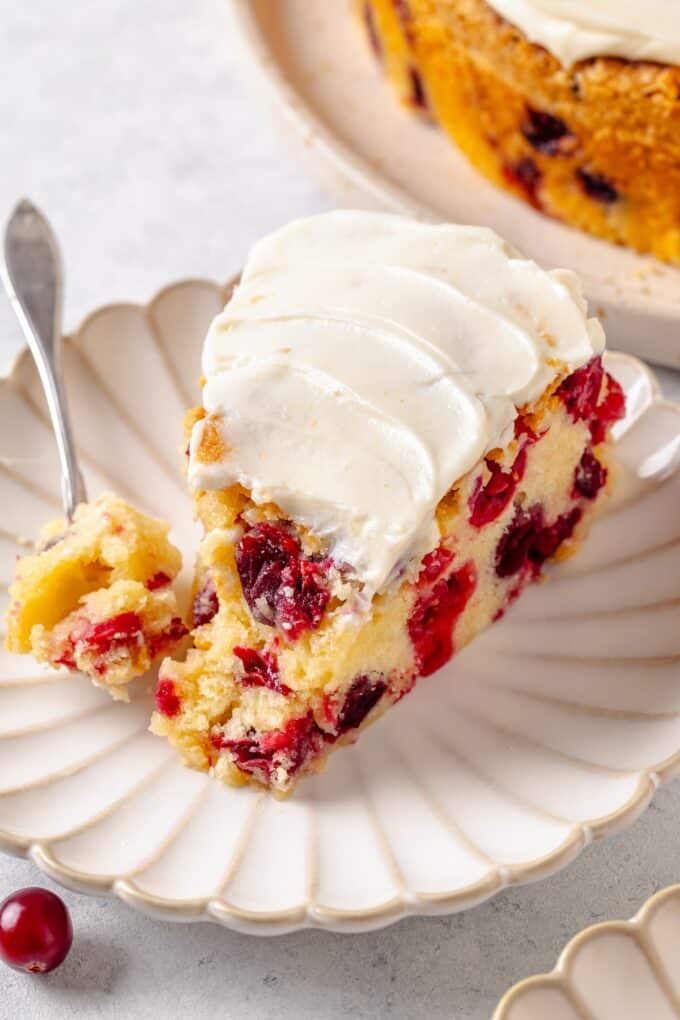 A fork resting with a bite of cranberry cake alongside a slice on a fluted round plate.
