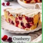 A slice of cranberry cake with cream cheese frosting on a small fluted round plate with cranberries scattered about and a green border and text around the photo.