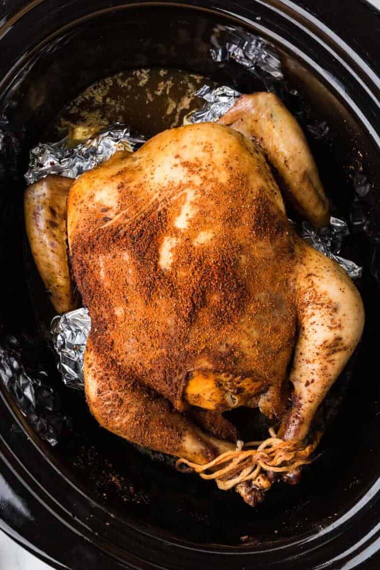 A seasoned and trussed whole chicken in a crock pot insert after being cooked.