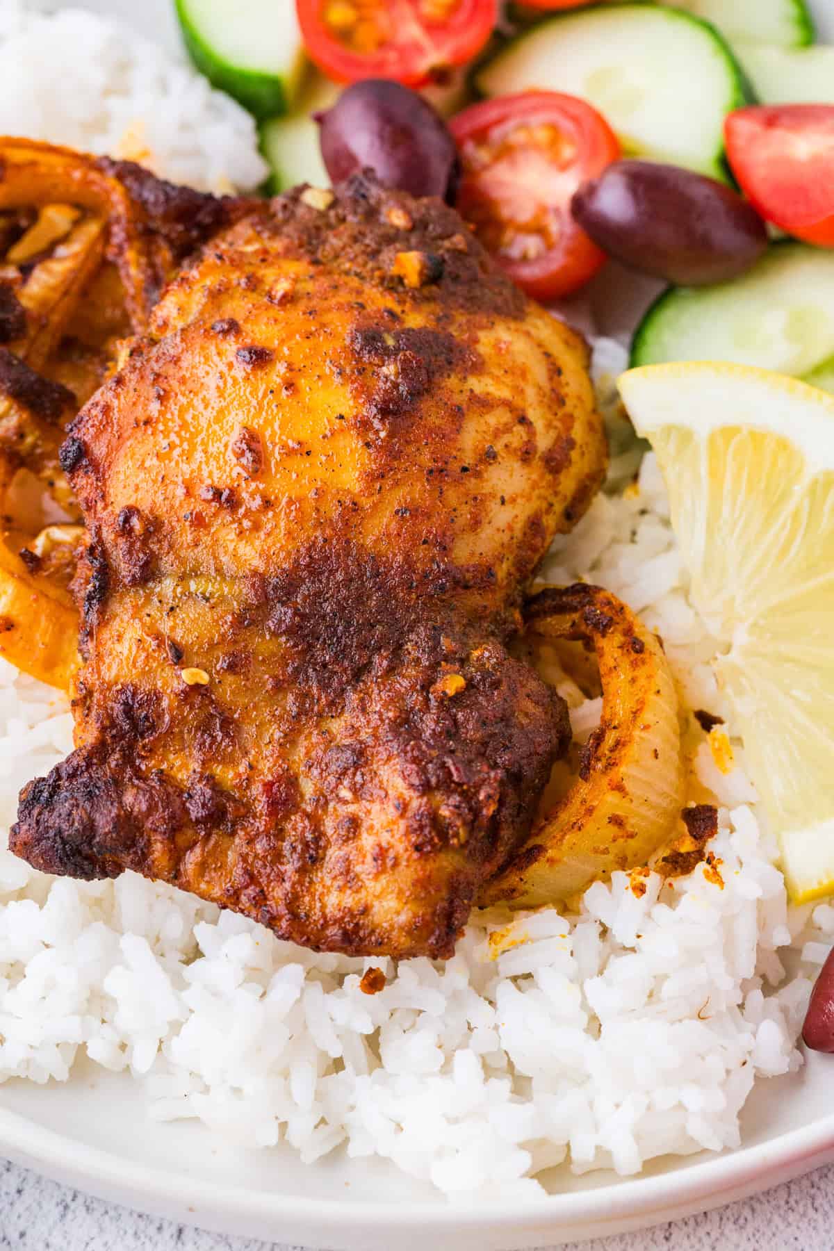 Close up of an oven roasted chicken shawarma thigh served over white rice with a lemon wedge to the side.