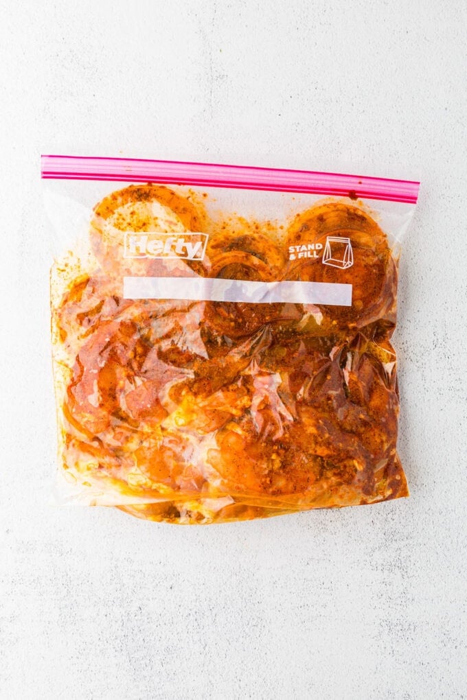 Chicken thighs and sliced onions being marinated in a plastic bag.