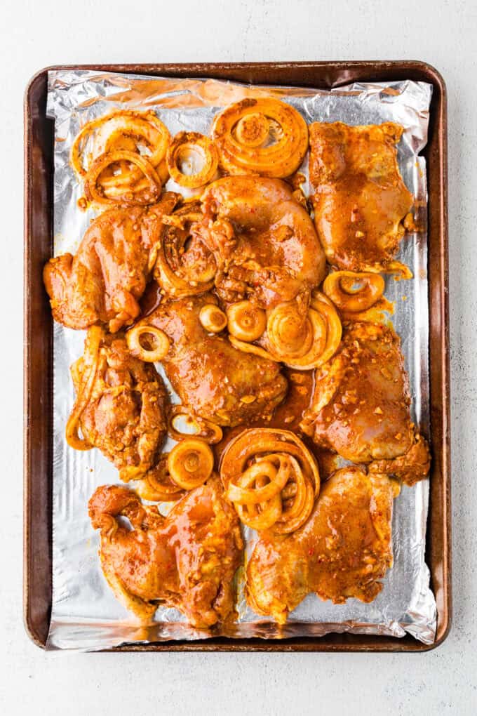 Marinated chicken thighs and onions on a foil lined baking sheet before being cooked.