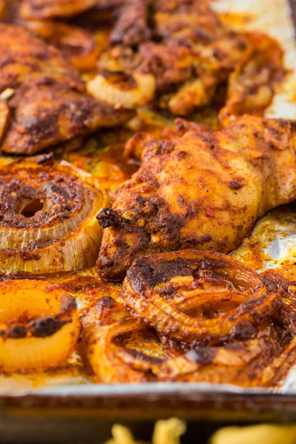 Close up of roasted onions and chicken thighs on a foil lined baking sheet.