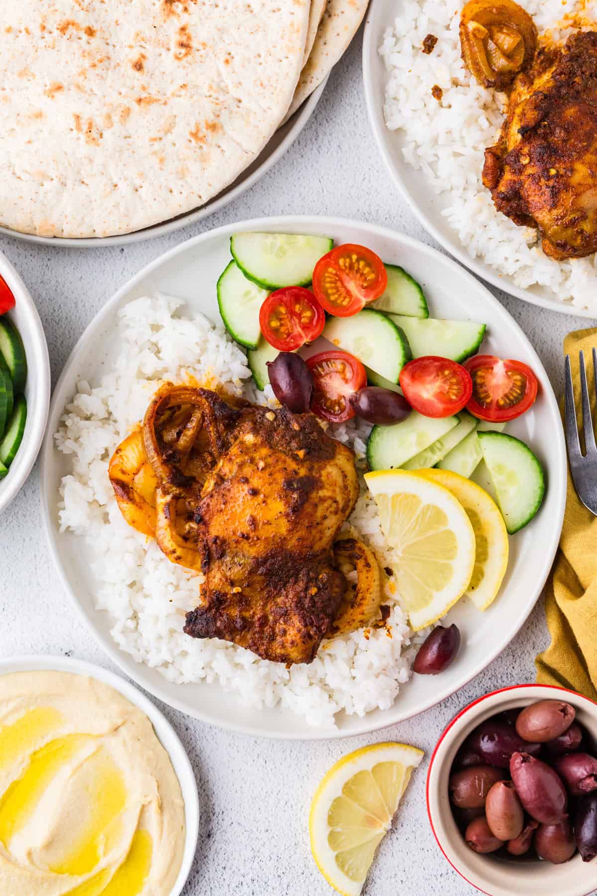 Round with plates with chicken shawarma served over white rice with a side of a veggie salad.
