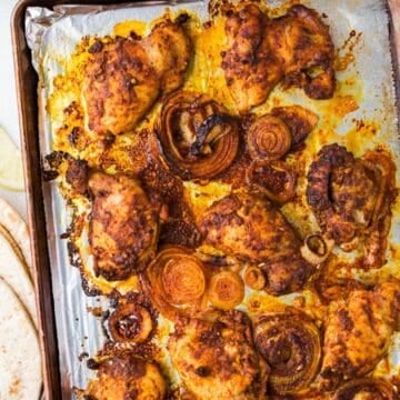 Close up of oven roasted chicken thighs and onions on a foil lined baking sheet.