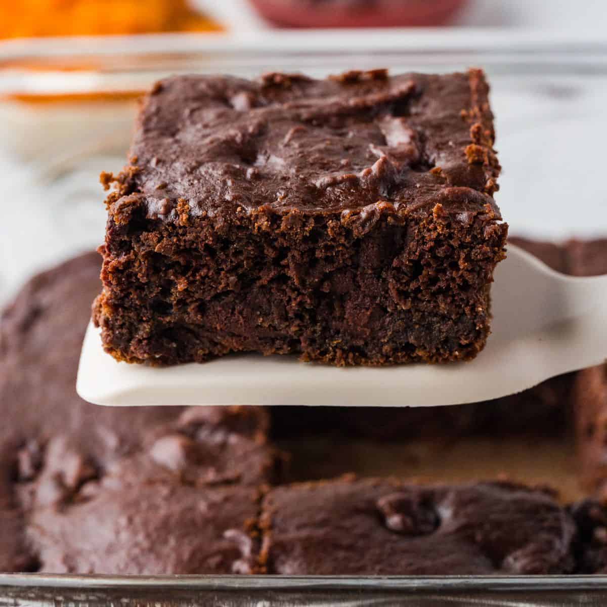 Close up of a square piece of chocolate pumpkin cake being lifted up from a baking dish.