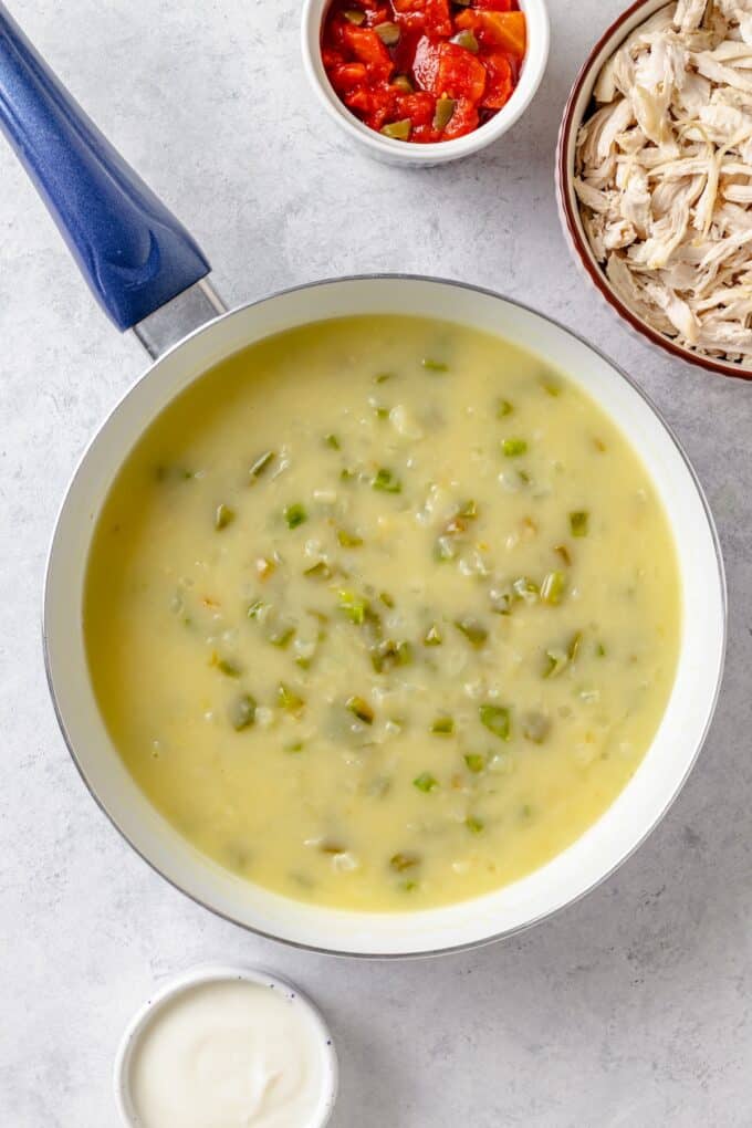 A brothy mixture with onions and green peppers in a white skillet.