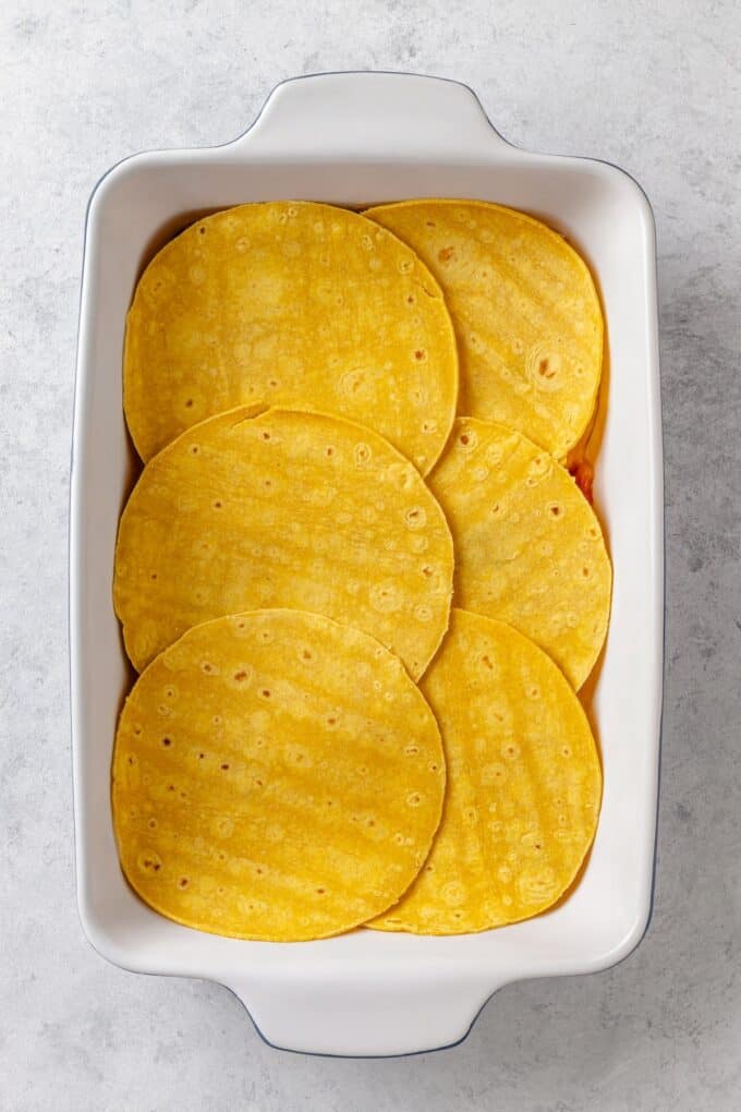 A rectangular white casserole dish with a layer of corn tortillas placed in it.