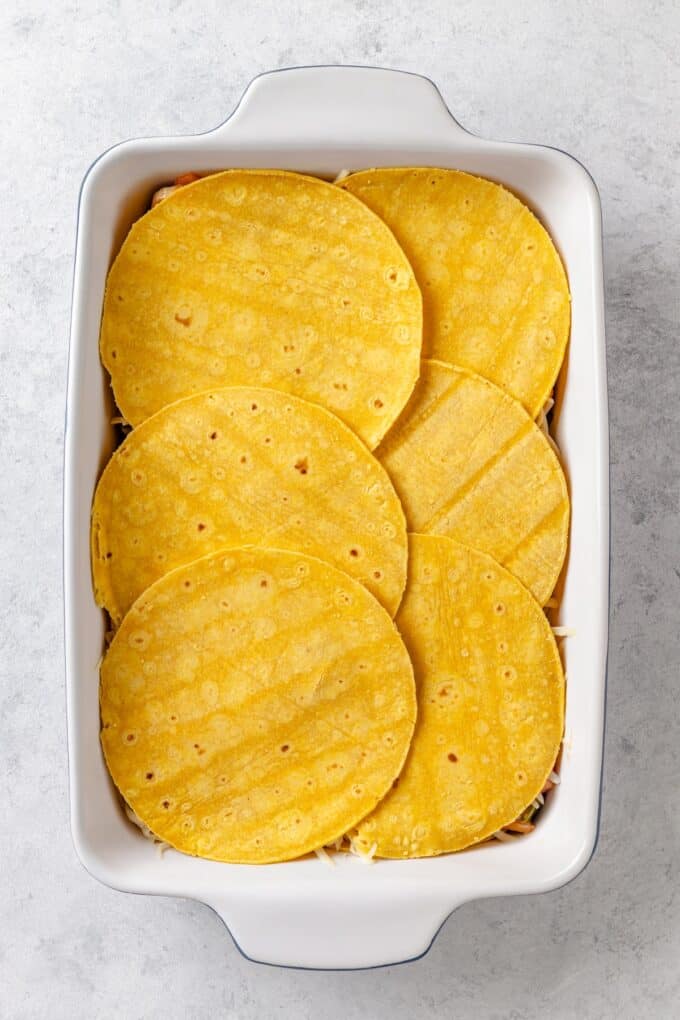 A rectangular white casserole dish with corn tortillas layered in it.