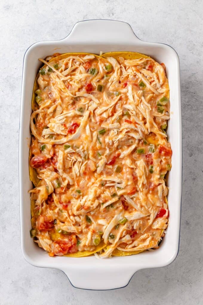 A creamy chicken and Rotel mixture with peppers and onions layered a second time on top of corn tortillas in a casserole dish.