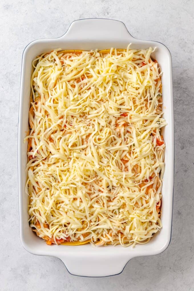 Shredded cheese covering a chicken and corn tortilla layered casserole in a white rectangular dish before being baked.