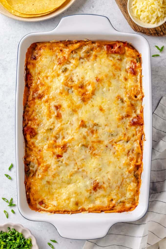 A cheesy baked casserole in a white rectangular dish with corn tortillas and green onions to the side.
