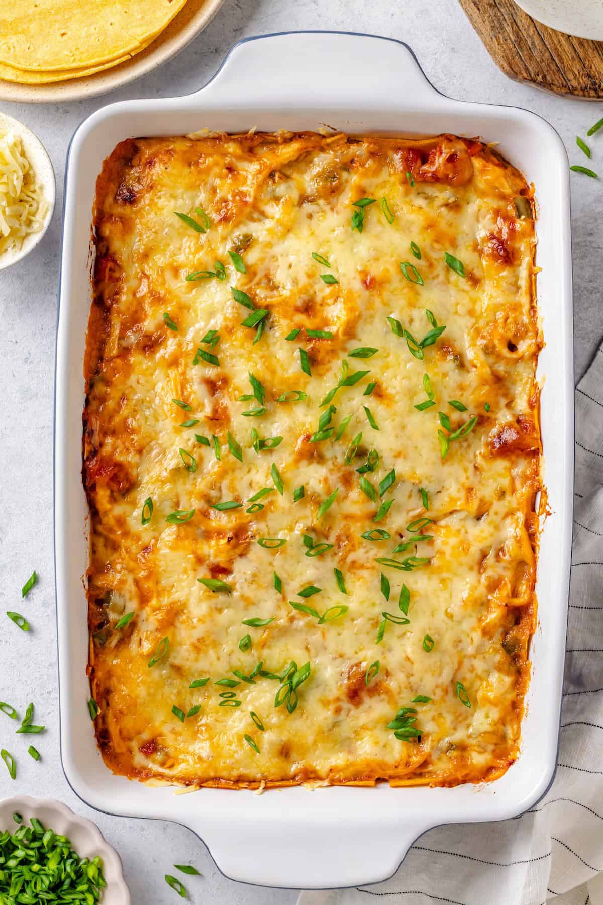 Sliced green onions sprinkled on top of a cheesy chicken tex mex casserole with corn tortilla layers.