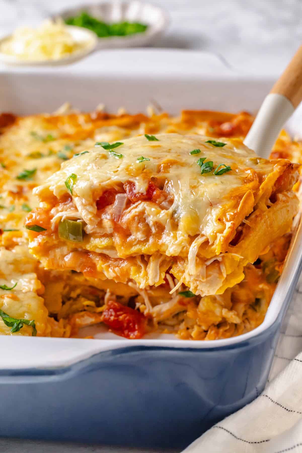 A spatula lifting up a square cut piece of a cheesy King Ranch chicken casserole from a blue and white baking dish.