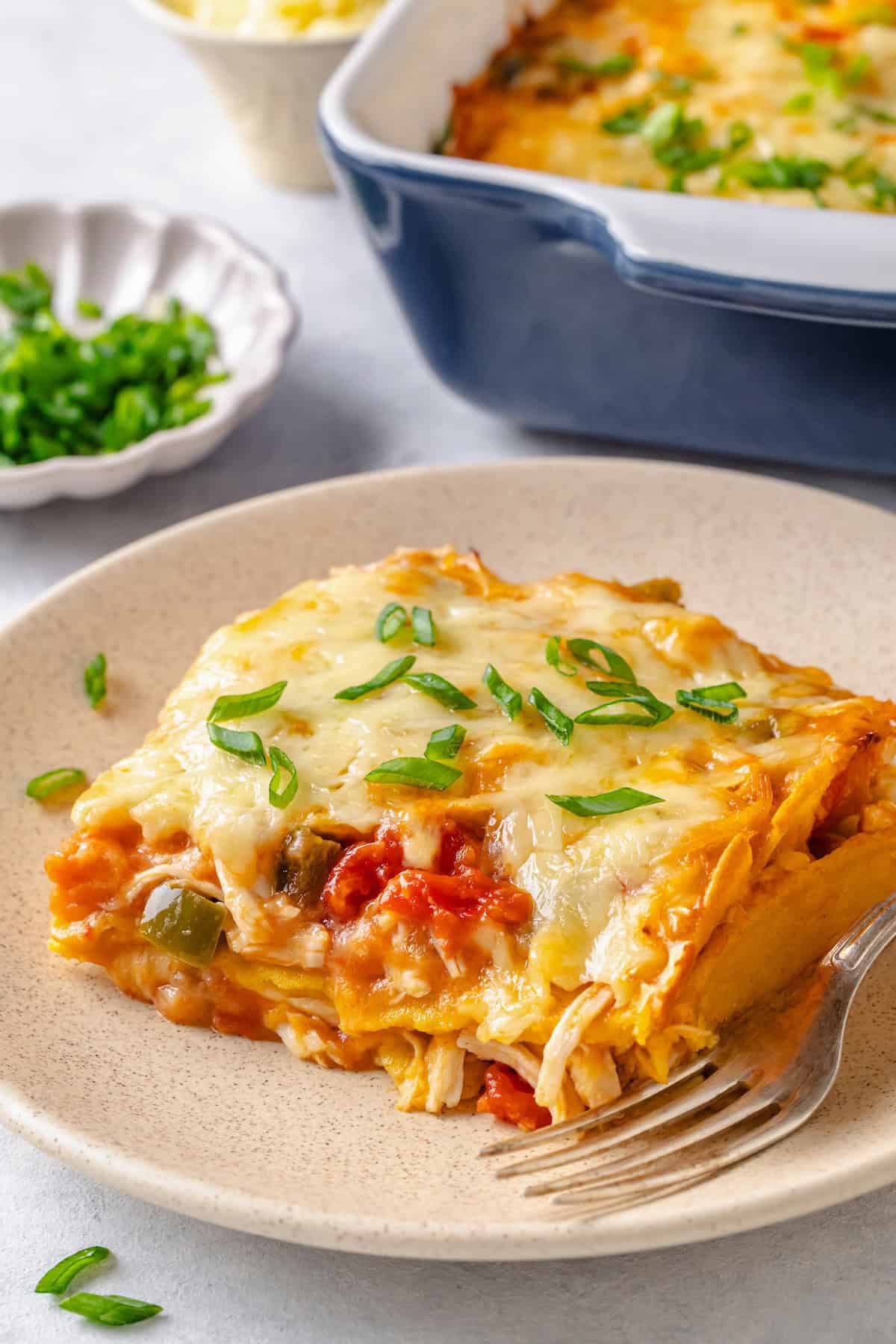 A serving of a layered cheesy chicken and tortilla casserole on a plate with a fork to the side.