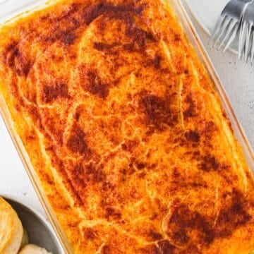 Close up of baked cheesy grits casserole in a clear baking dish with biscuits to the side.