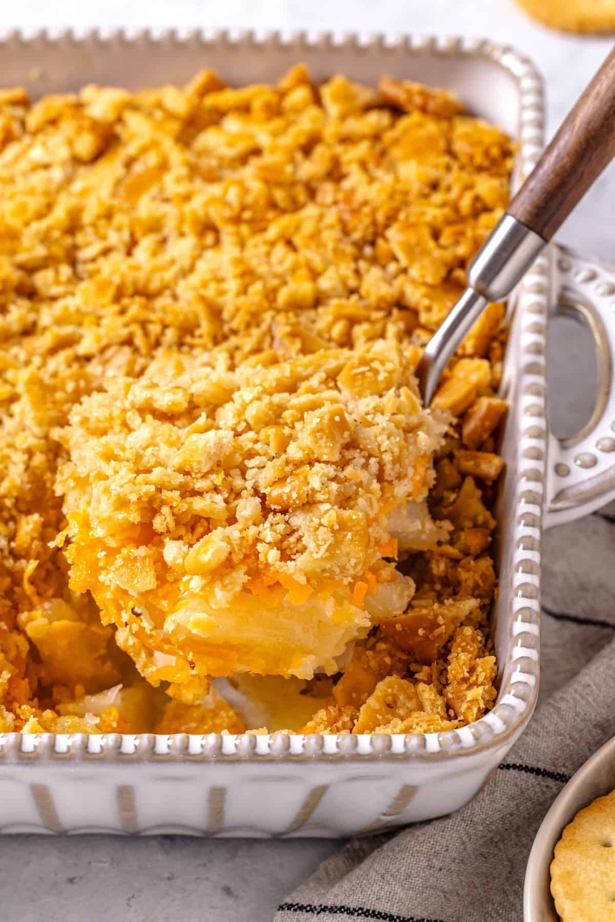 A spoon lifting up a scoop of pineapple casserole from a white baking dish.