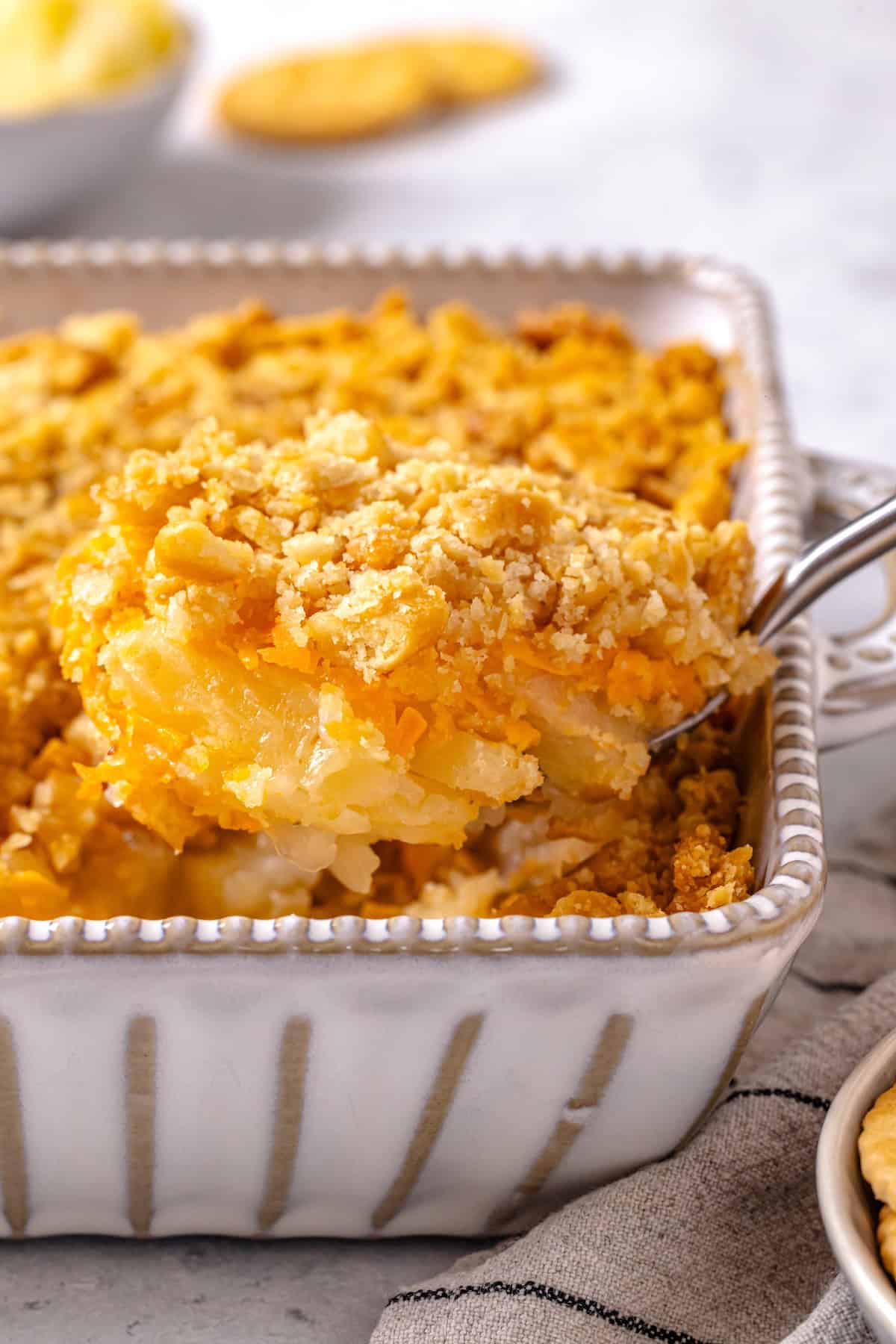 A spoon lifting up a scoop of pineapple casserole with a layer of cheddar cheese and buttery crushed crackers on top.