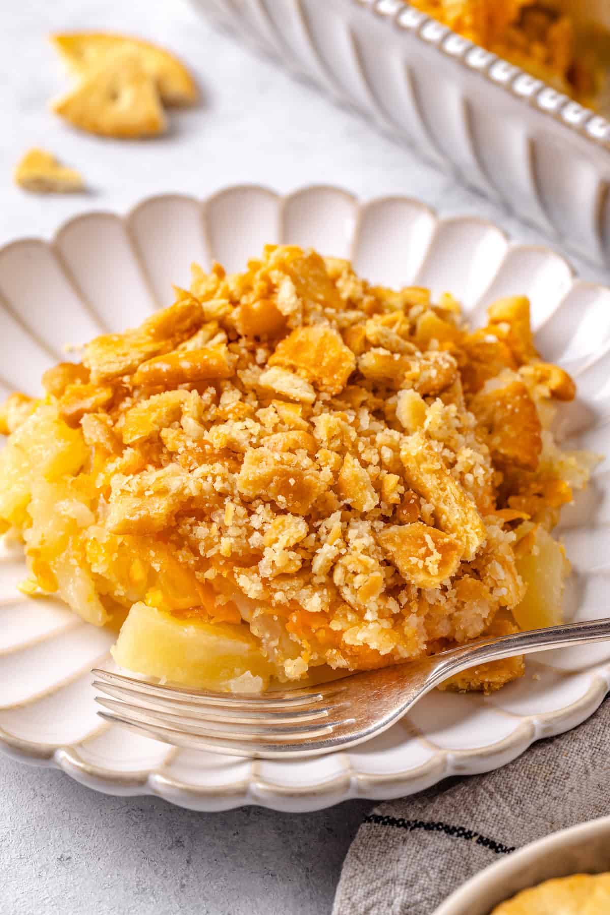 A serving of pineapple casserole with cheese and crackers on a fluted plate with a fork resting on it.