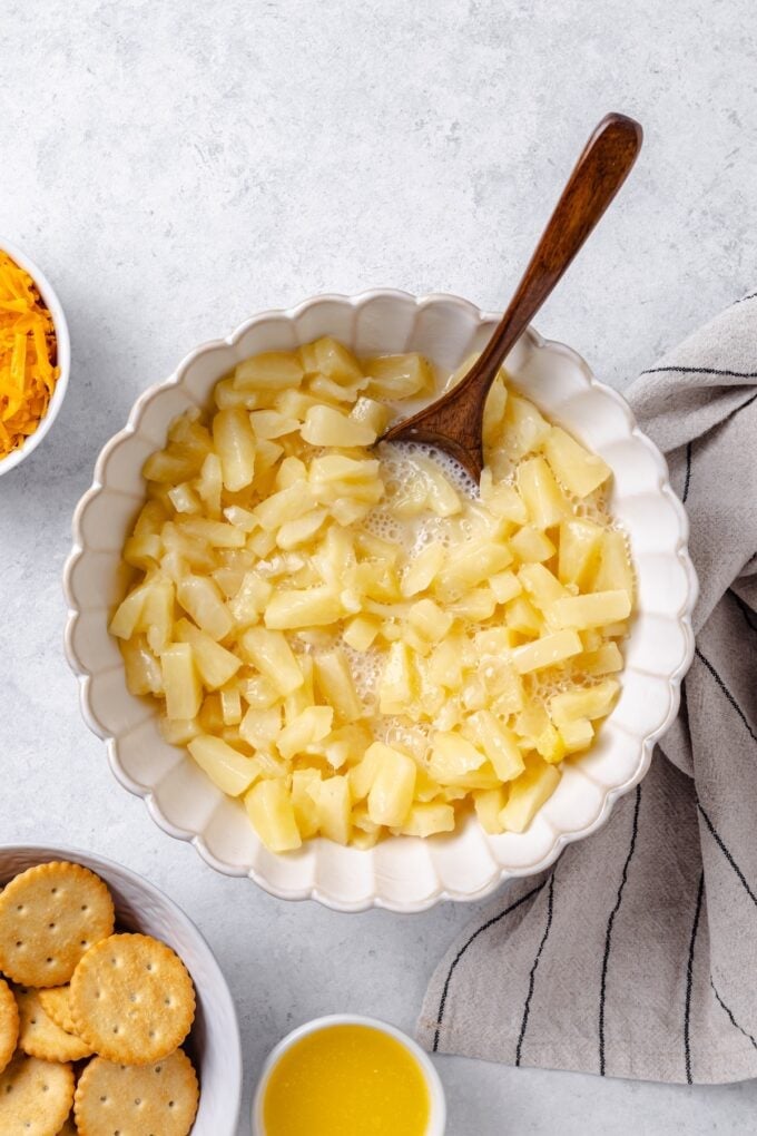 Canned pineapple chunks in a syrupy mixture in a bowl with a wooden spoon resting in it.