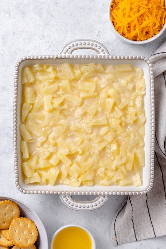 A white square casserole dish filled with pineapple chunks in a syrupy mixture.