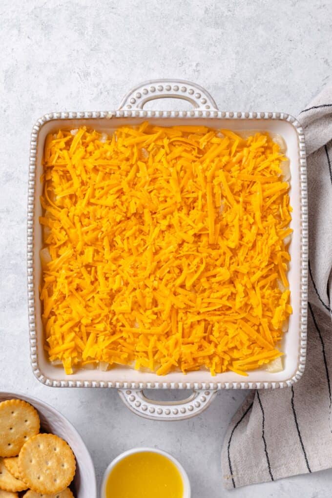 Shredded cheddar cheese sprinkled on top of a pineapple mixture in a white casserole dish.