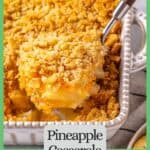 A spoon lifting up a scoop of pineapple casserole from a white baking dish with a green border and text around the photo.