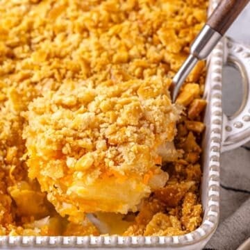 Close up of a spoon lifting up a scoop of pineapple casserole from a white baking dish.