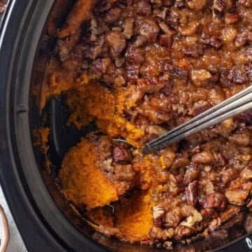 A spoon resting in a slow cooker with a sweet potato casserole with a nutty streusel topping.