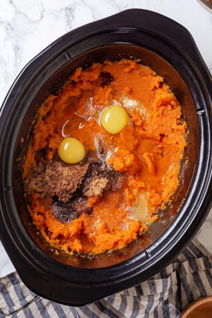 A slow cooker insert with mashed sweet potatoes topped with cracked eggs, sugar, melted butter, vanilla and seasonings.