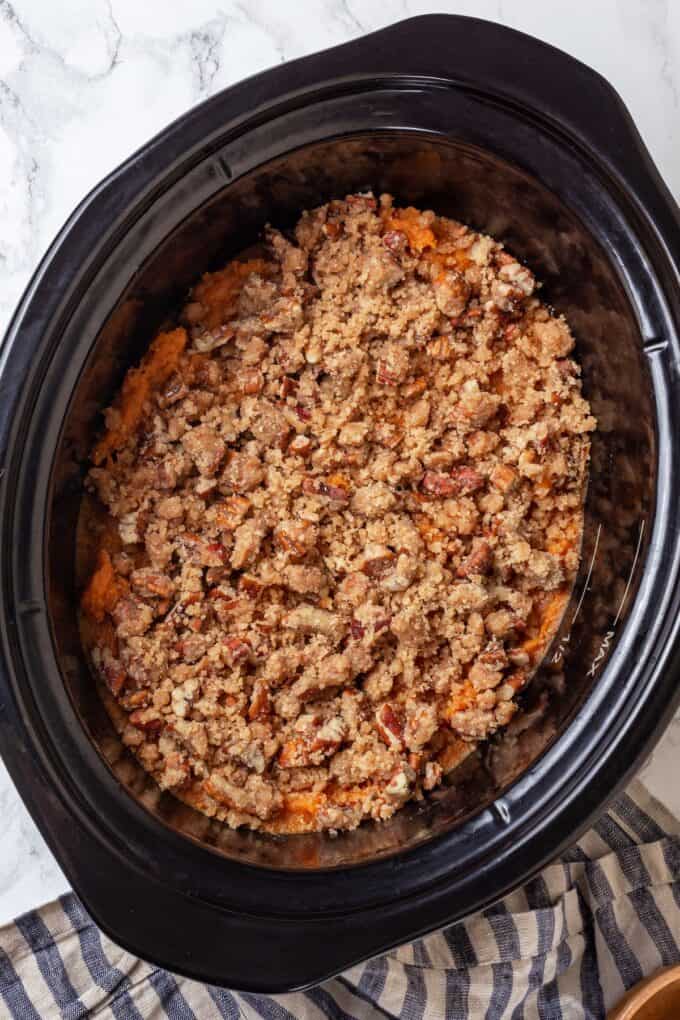 A nutty streusel topping on top of a layer of mashed potatoes in a slow cooker before being cooked.
