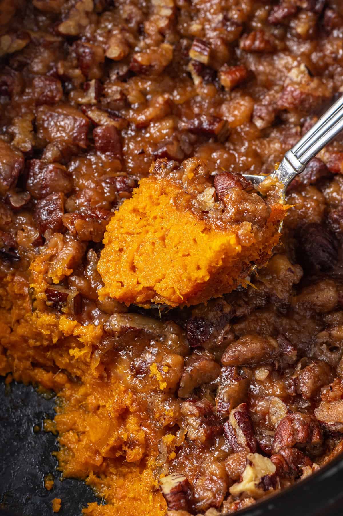 A spoon lifting up a scoop of a sweet potato casserole cooked in a crock pot.
