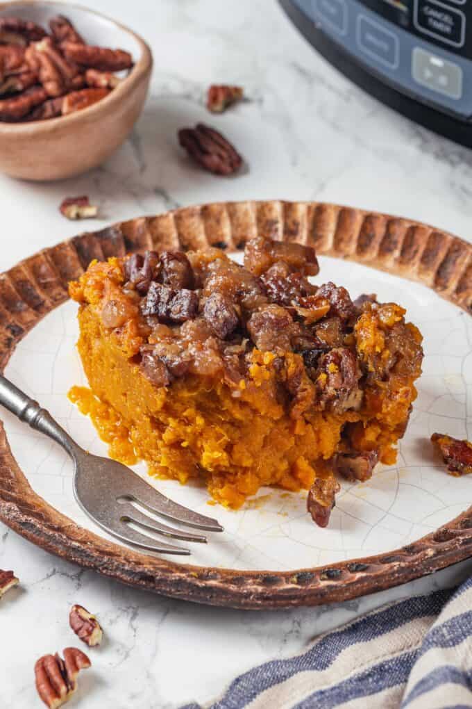 A serving of sweet potato casserole with buttery pecans on top served on a plate with a fork to the side.